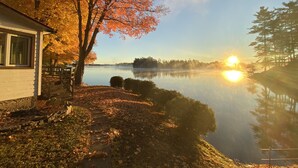 A lakeside property with a wooden dock, a house with a visible window, and a clear view of the lake and surrounding trees. - Cozy Lakefront Getaway in South Frontenac, Rustic & Elegant, Highspeed Internet (Battersea)