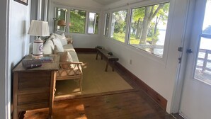 A spacious room with a high ceiling, large windows, a wooden floor, a sofa, a small table, and a lamp. - Cozy Lakefront Getaway in South Frontenac, Rustic & Elegant, Highspeed Internet (Battersea)