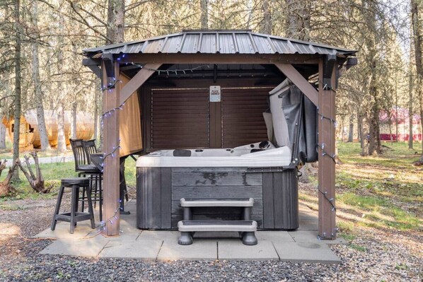 A hot tub with a wooden structure, a bench, and a sign indicating it is a shower area. - Rustic Cozy Cabin with hot tub (Bragg Creek)