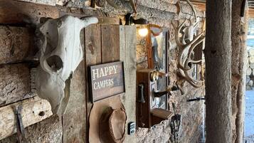 Un intérieur rustique avec un mur en bois, un crâne accroché au mur, une pancarte sur laquelle on peut lire « ICI HABITENT DES CAMPEURS HEUREUX », et un chapeau suspendu au mur.