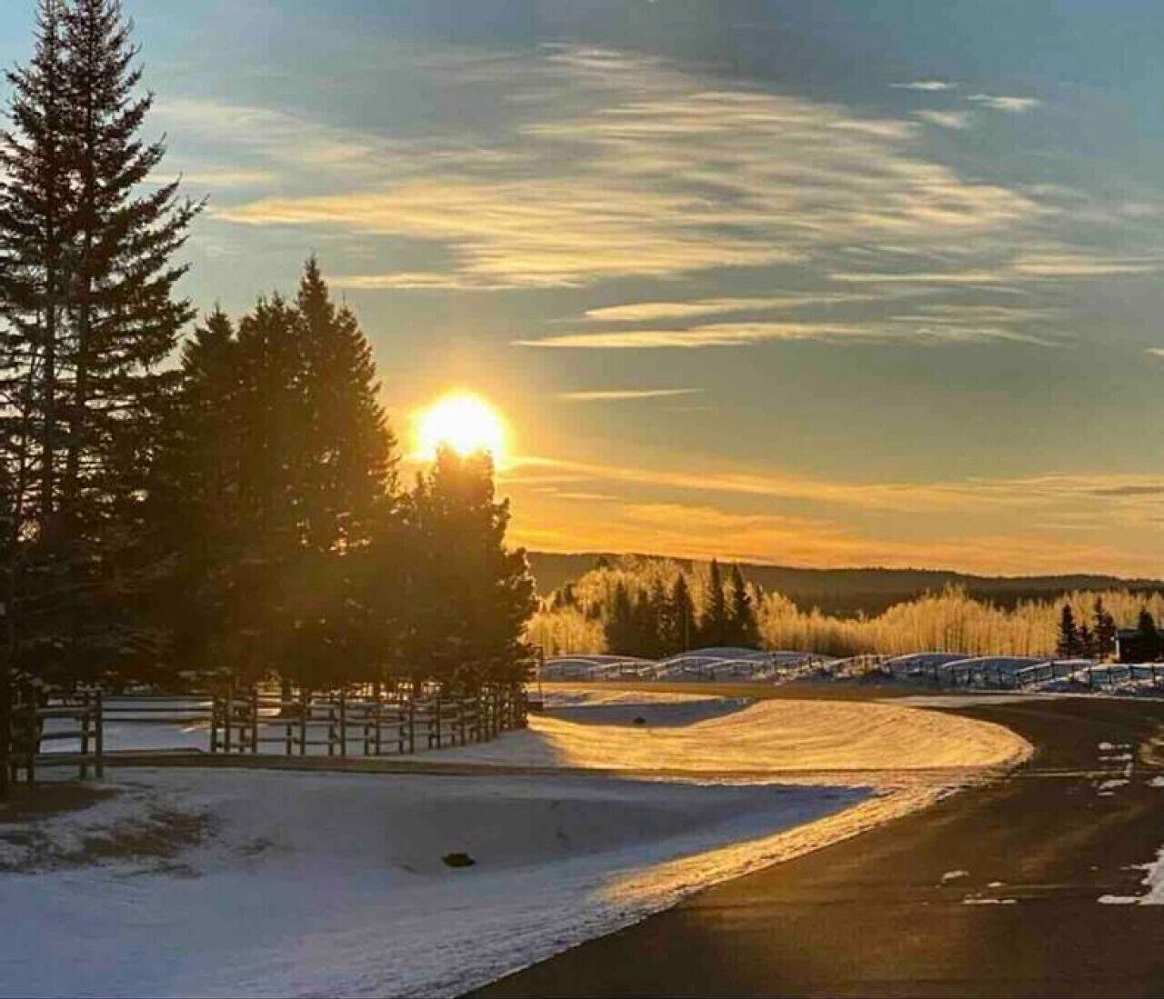 A snowy landscape with a road curving through a forest at sunset.