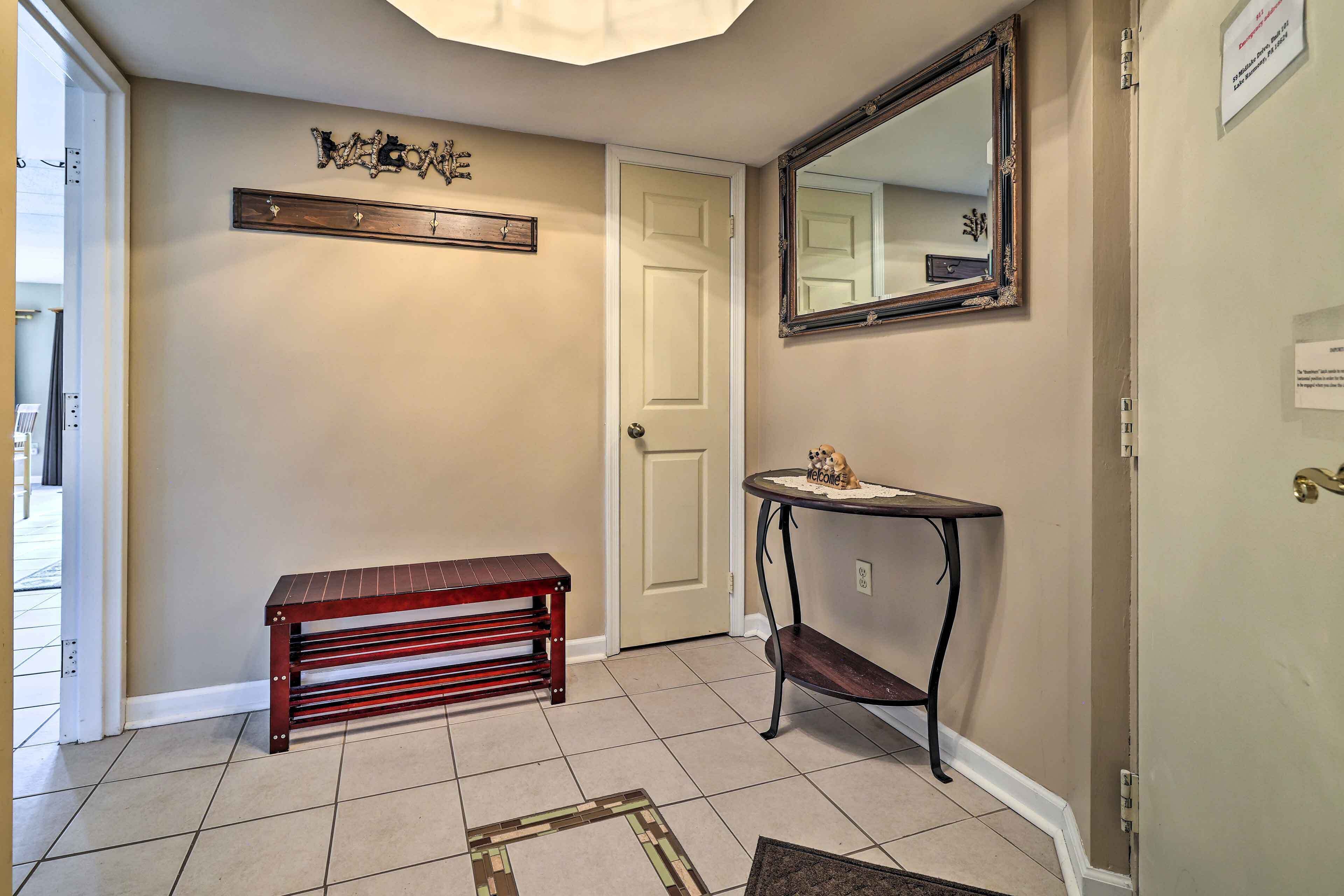 A hallway with a wooden bench, a small table with a decorative item, a mirror, and a welcome sign on the wall.