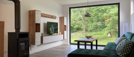 A modern living room with a large window, a fireplace, a green sofa, and a wooden table.