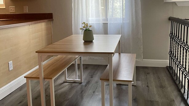 Een eetruimte met een houten tafel en banken, een kroonluchter en een raam met lichte gordijnen.
