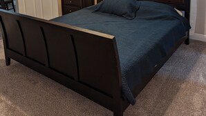 Een slaapkamer met een donker houten bed, een plafondventilator, een bedlampje en een deur.