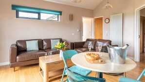 A cozy living room with a brown leather sofa, a wooden coffee table, and a round table with a metal bucket. - Buttercup lodge - sleeps 4/5 with hot tub & countryside views (Cheddar)
