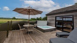 An outdoor deck with a hot tub, a table with chairs, and a large umbrella. - Buttercup lodge - sleeps 4/5 with hot tub & countryside views (Cheddar)