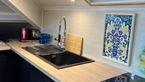A modern kitchen with a black sink, wooden countertop, and a backsplash with a blue and white tile design. - Apartment T LUXE (Pierrefitte-sur-Seine)