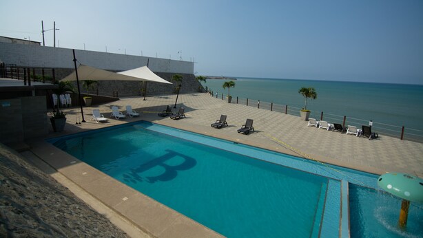 Une piscine ornée du logo « B », des chaises longues, un espace ombragé et une vue sur l’océan.