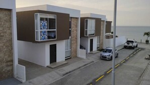 Une rue résidentielle moderne bordée de maisons contemporaines, offrant une vue dégagée sur l’océan, et où est garé un pick-up blanc.