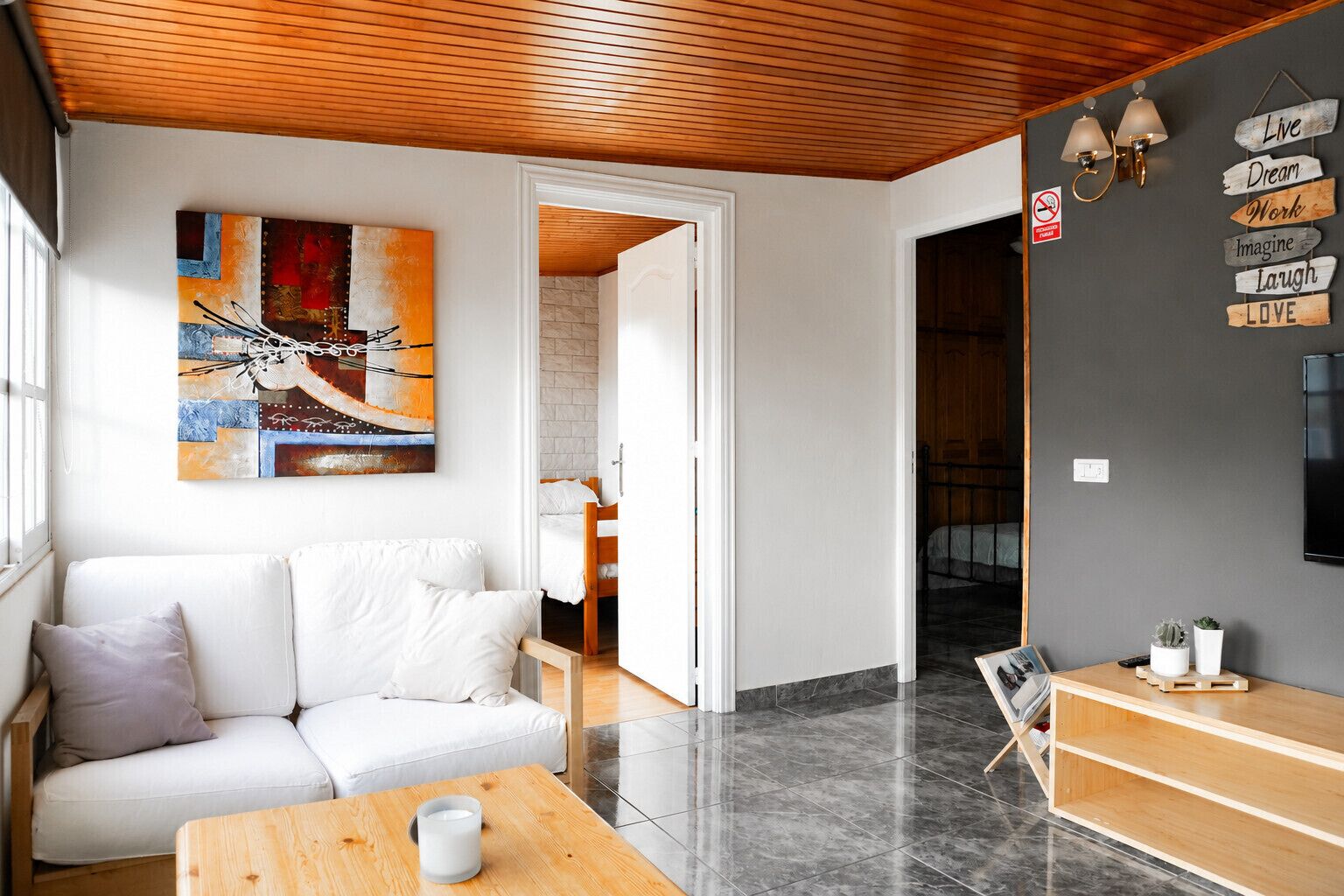 A modern living room with a white sofa, a wooden coffee table, and a painting on the wall.