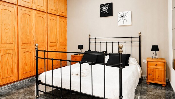 A bedroom with a metal bed frame, wooden wardrobe, two bedside tables with lamps, and artwork on the wall. - Nue Apartment · Terrace & Views Near Las Teresitas (Santa Cruz de Tenerife)