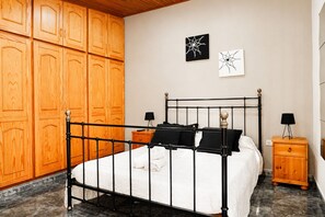 A bedroom with a metal bed frame, wooden wardrobe, two bedside tables with lamps, and artwork on the wall.
