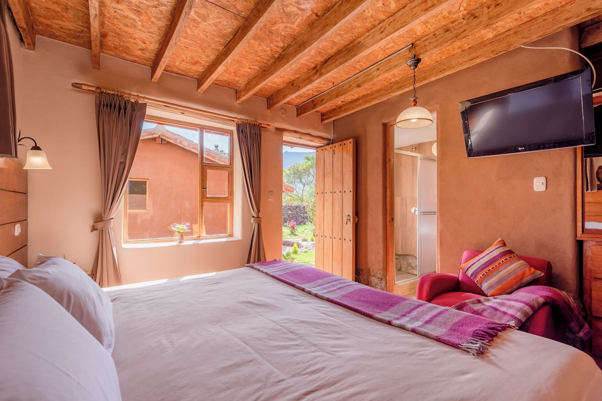 A bedroom with a large bed, a TV mounted on the wall, and a window with curtains.