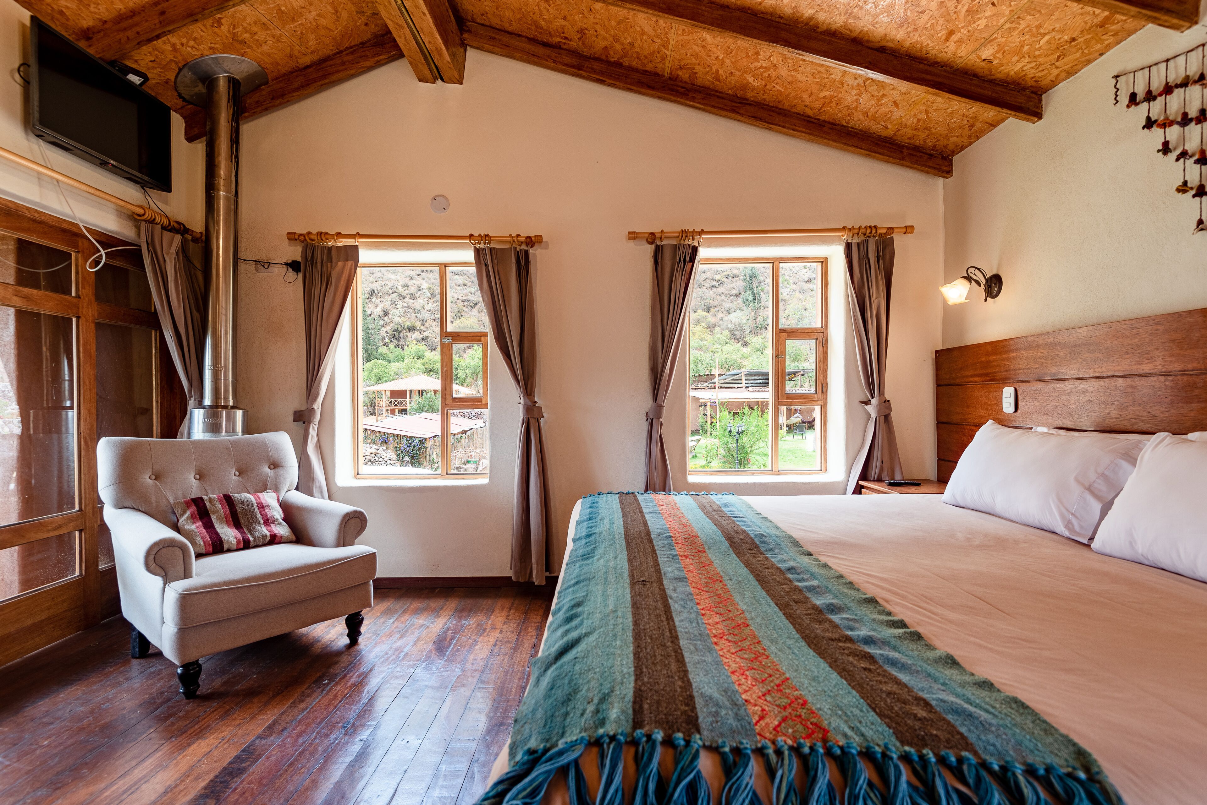 A bedroom with a large bed, a wooden headboard, a chair with a cushion, and a window with curtains.