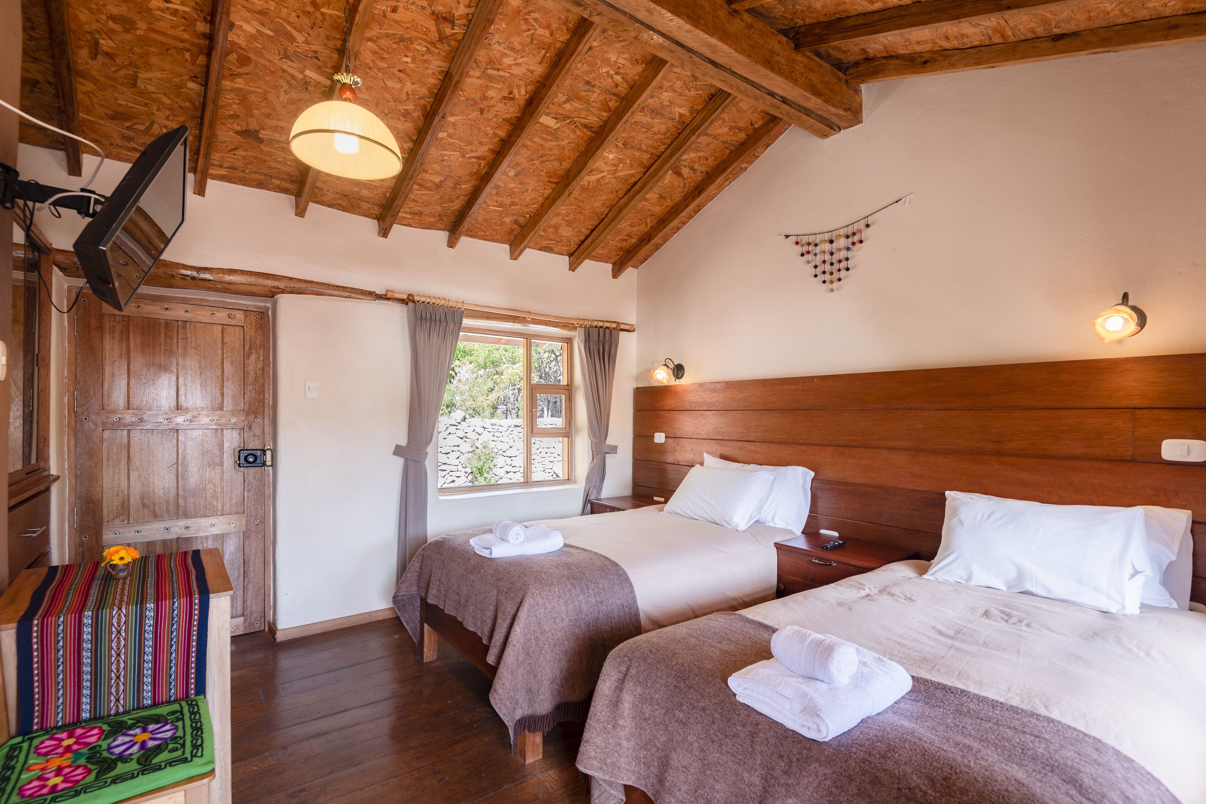 A room with two beds, wooden beams, a television, and a window with curtains.