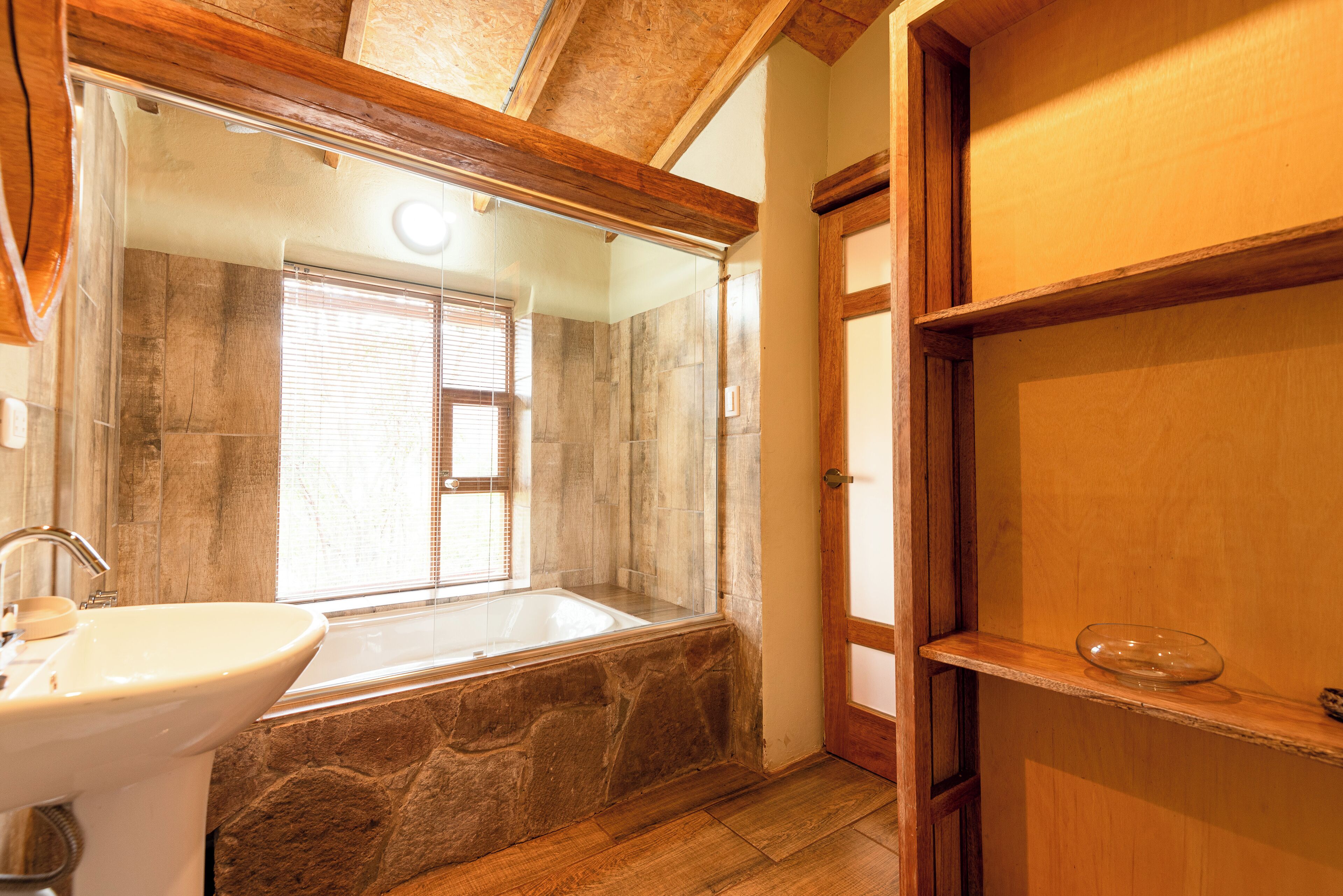 A bathroom with a stone sink, a bathtub, and a wooden shelf.