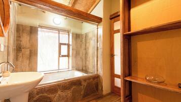 A bathroom with a stone sink, a bathtub, and a wooden shelf.