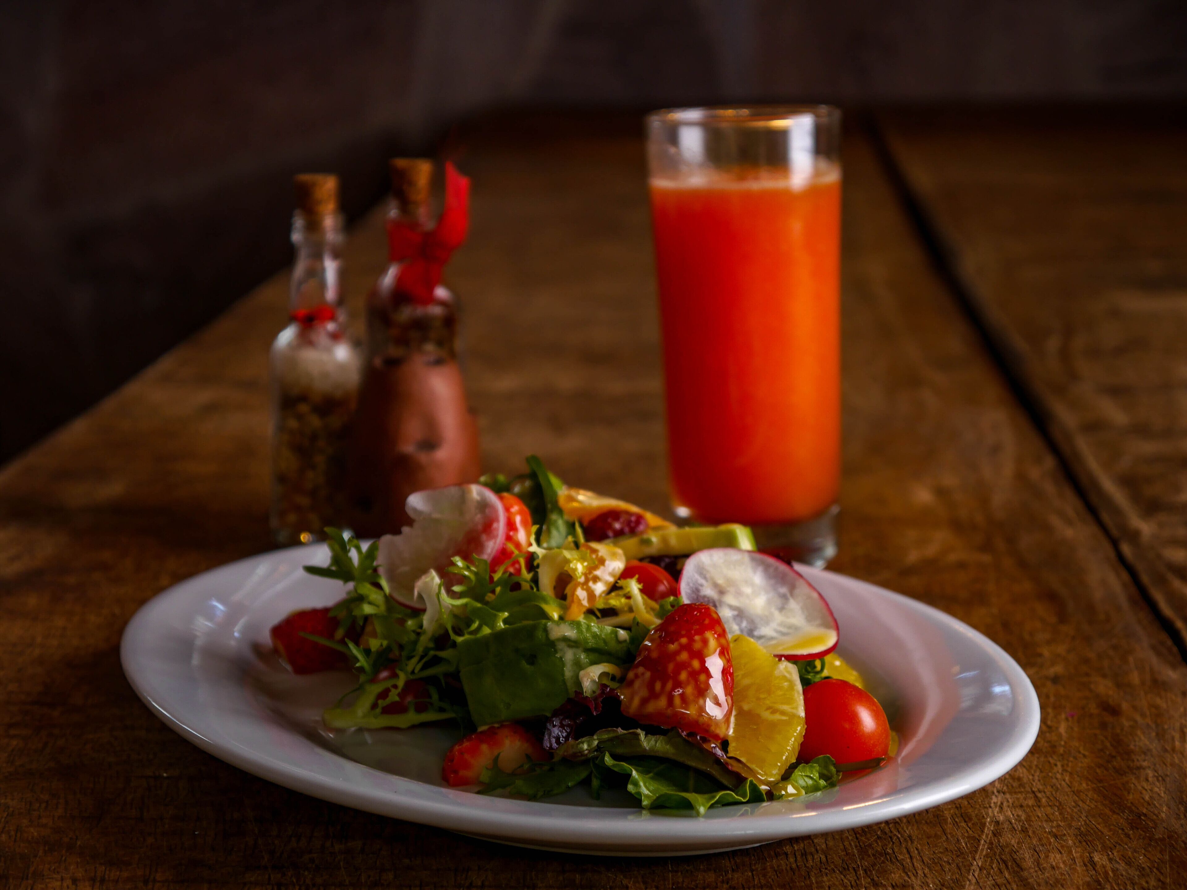 A plate of salad with various vegetables and a glass of red juice on a wooden table.