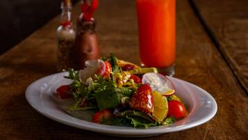 A plate of salad with various vegetables and a glass of red juice on a wooden table.