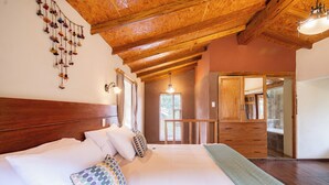 Une chambre avec un plafond en bois, un grand lit avec une literie blanche, une commode en bois et une vue sur un balcon.