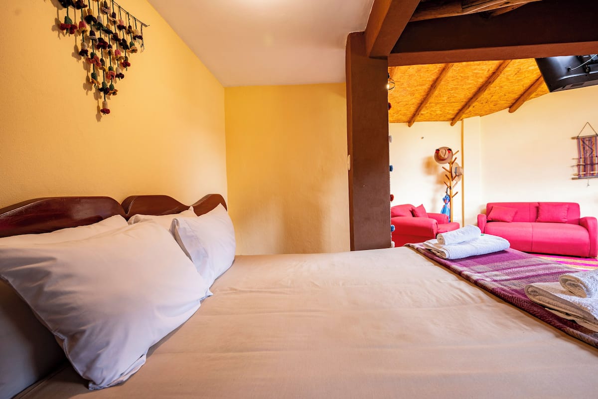 A hotel room with a bed, pillows, a red sofa, and a wall decoration.