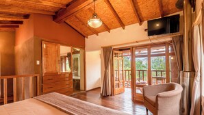 Une chambre spacieuse avec un grand lit, des poutres apparentes en bois au plafond, une télévision et une vue sur l’extérieur grâce à une porte-fenêtre coulissante.