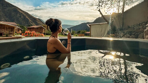Une personne se détend dans un bain à remous, avec une vue sur les montagnes et les maisons.