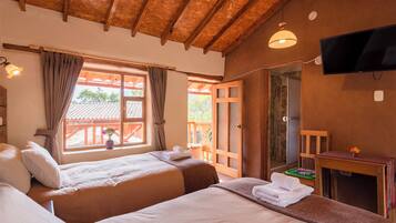 A hotel room with two beds, a wooden ceiling, a TV, and a window with curtains.