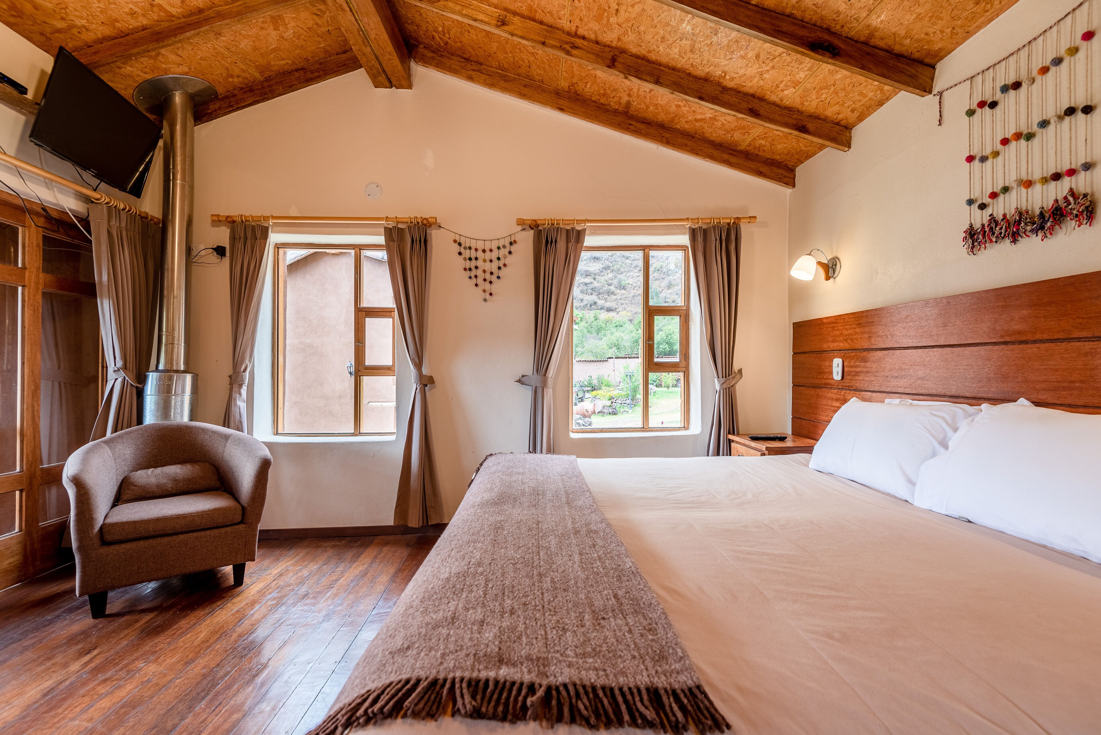 A bedroom with a bed, a chair, a wooden ceiling, and a window with curtains.