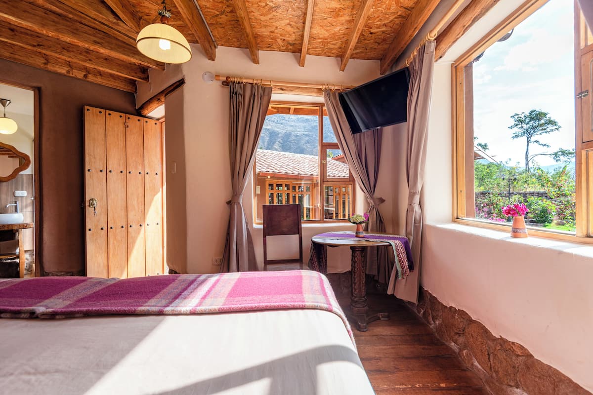 A bedroom with a bed, a small table, and a window with curtains.
