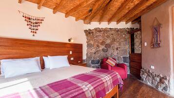 Quarto com teto de madeira, parede de pedra, cama com lençóis brancos e manta xadrez.