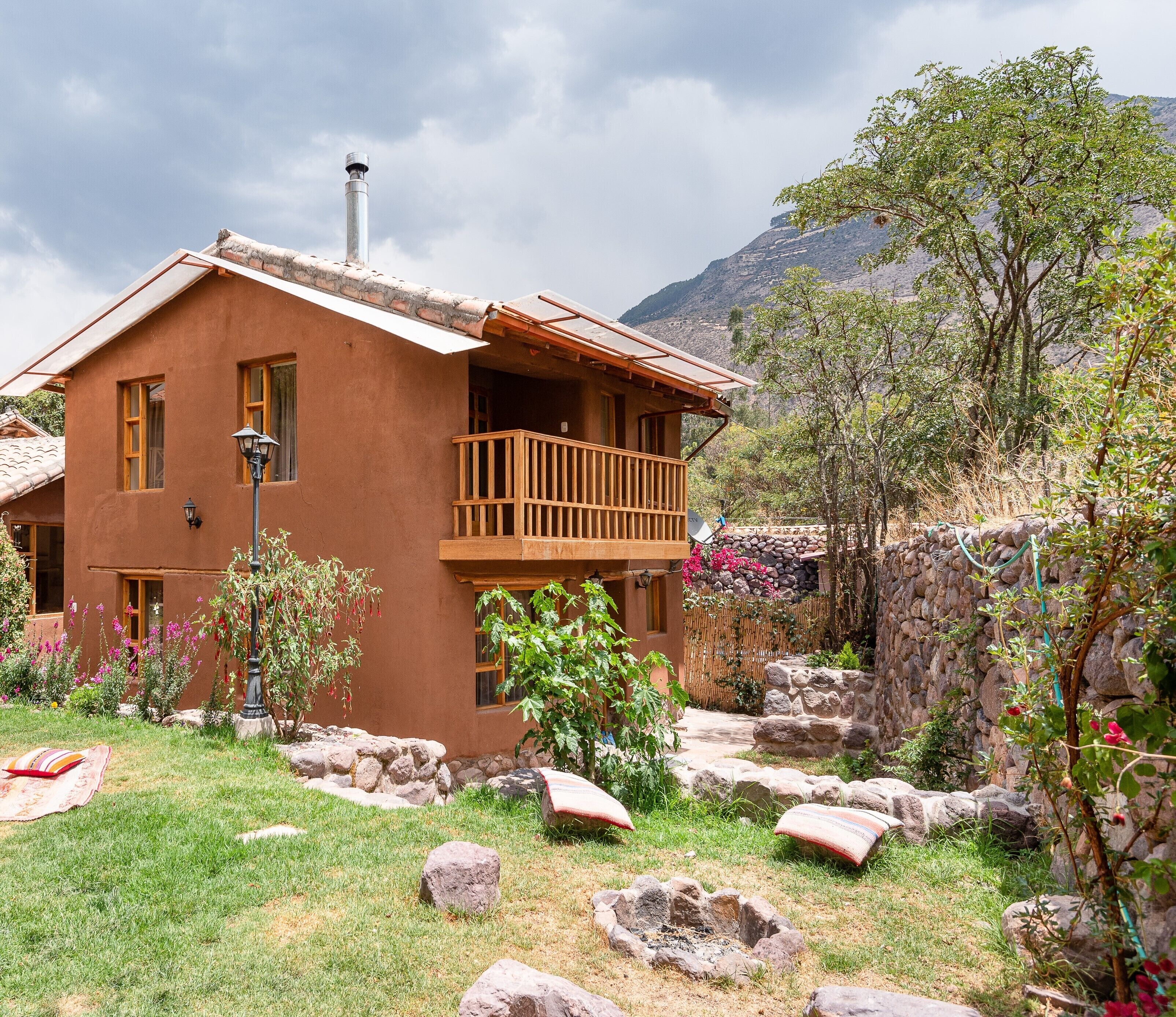 A two-story house with a balcony, surrounded by a garden with rocks and plants.