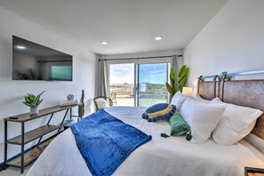 Een moderne hotelkamer met een groot bed, een bureau met een computer, een aan de muur bevestigde televisie en uitzicht op het omliggende landschap.
