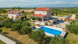 Una casa de dos pisos con piscina, rodeada de follaje y un cielo despejado.