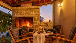 Un rincón exterior acogedor con una chimenea de piedra, sillas de madera y una mesa lista para comer.