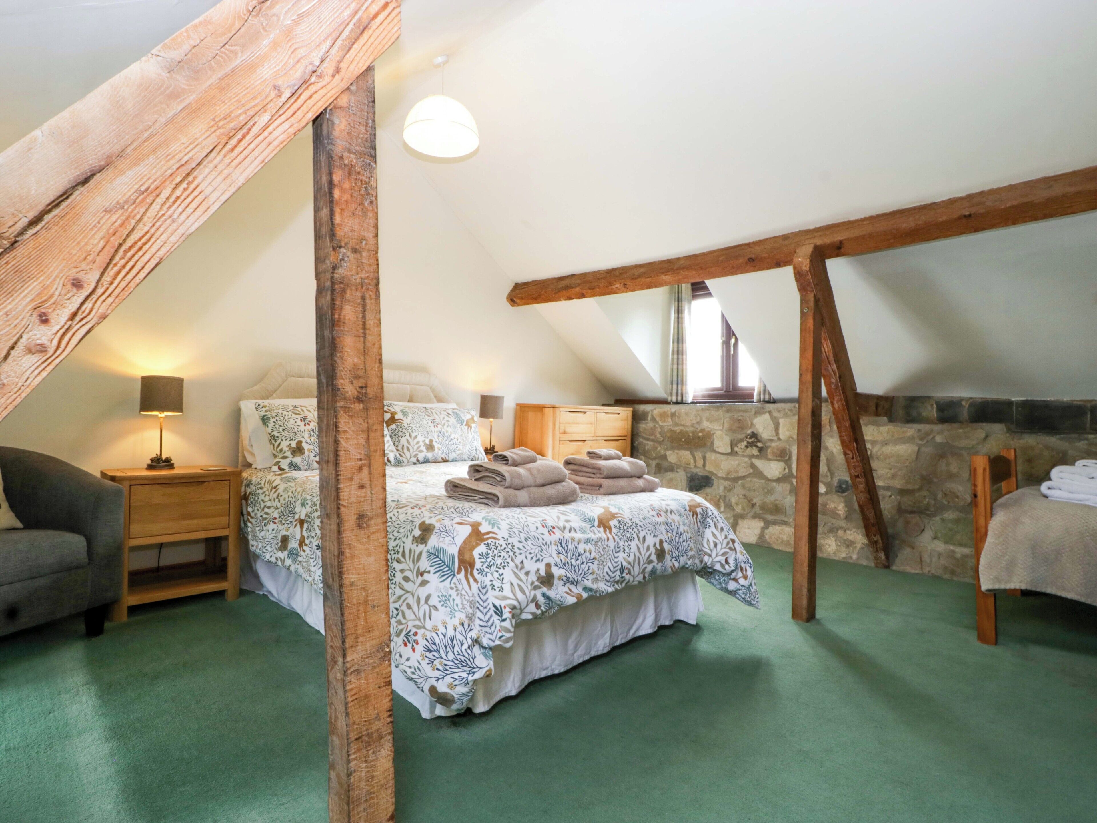 A cozy attic bedroom with a bed, a nightstand, a lamp, and a stone wall.