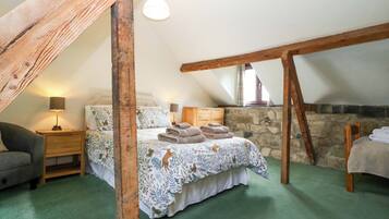 A cozy attic bedroom with a bed, a nightstand, a lamp, and a stone wall.