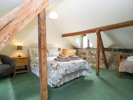 Un dormitorio acogedor en el ático con cama, mesita de noche, lámpara y pared de piedra.