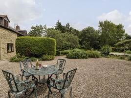 Un patio jardín con mesa y sillas, rodeado de grava y follaje.