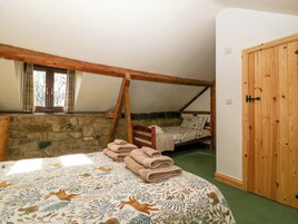Un dormitorio con techo inclinado, pared de piedra, estructura de cama de madera y armario de madera.