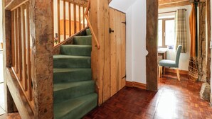 Een houten trap met een groen tapijt, een houten deur en een uitzicht op een eetruimte met een tafel en stoelen.