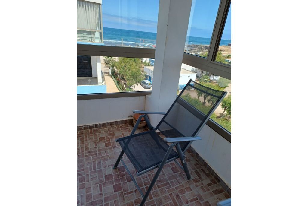 Uma varanda com vista para o oceano, uma cadeira e piso de azulejos.