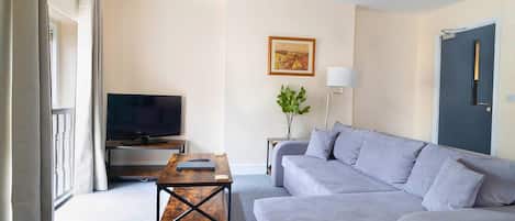 A modern living room with a grey sofa, a coffee table, a flat-screen TV, a lamp, and a framed picture on the wall.
