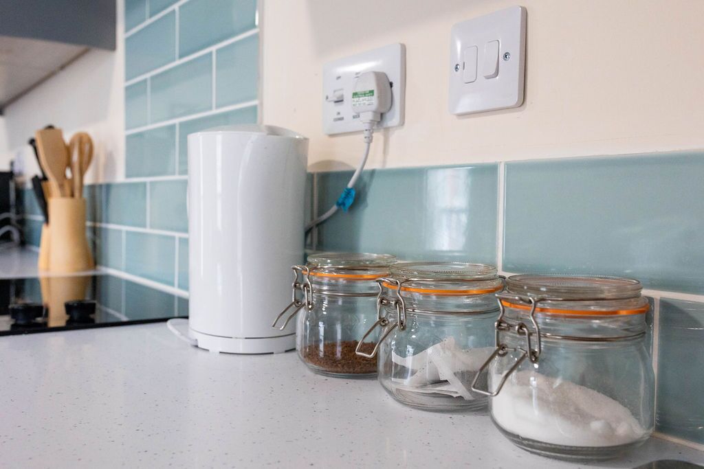A kitchen counter with a white appliance, three glass jars with metal lids, and a power outlet with a blue cord.