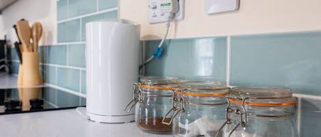 A kitchen counter with a white appliance, three glass jars with metal lids, and a power outlet with a blue cord.