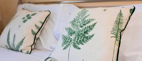 A bed with white bedding and two pillows with green fern embroidery.