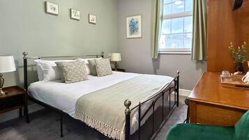 A neatly arranged bedroom with a bed, bedside tables, a desk, and a chair.