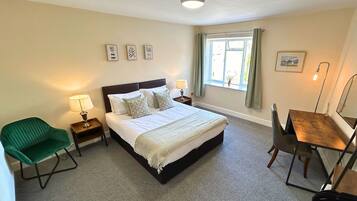 A bedroom with a bed, bedside tables, a chair, a desk, a window with curtains, and wall art.
