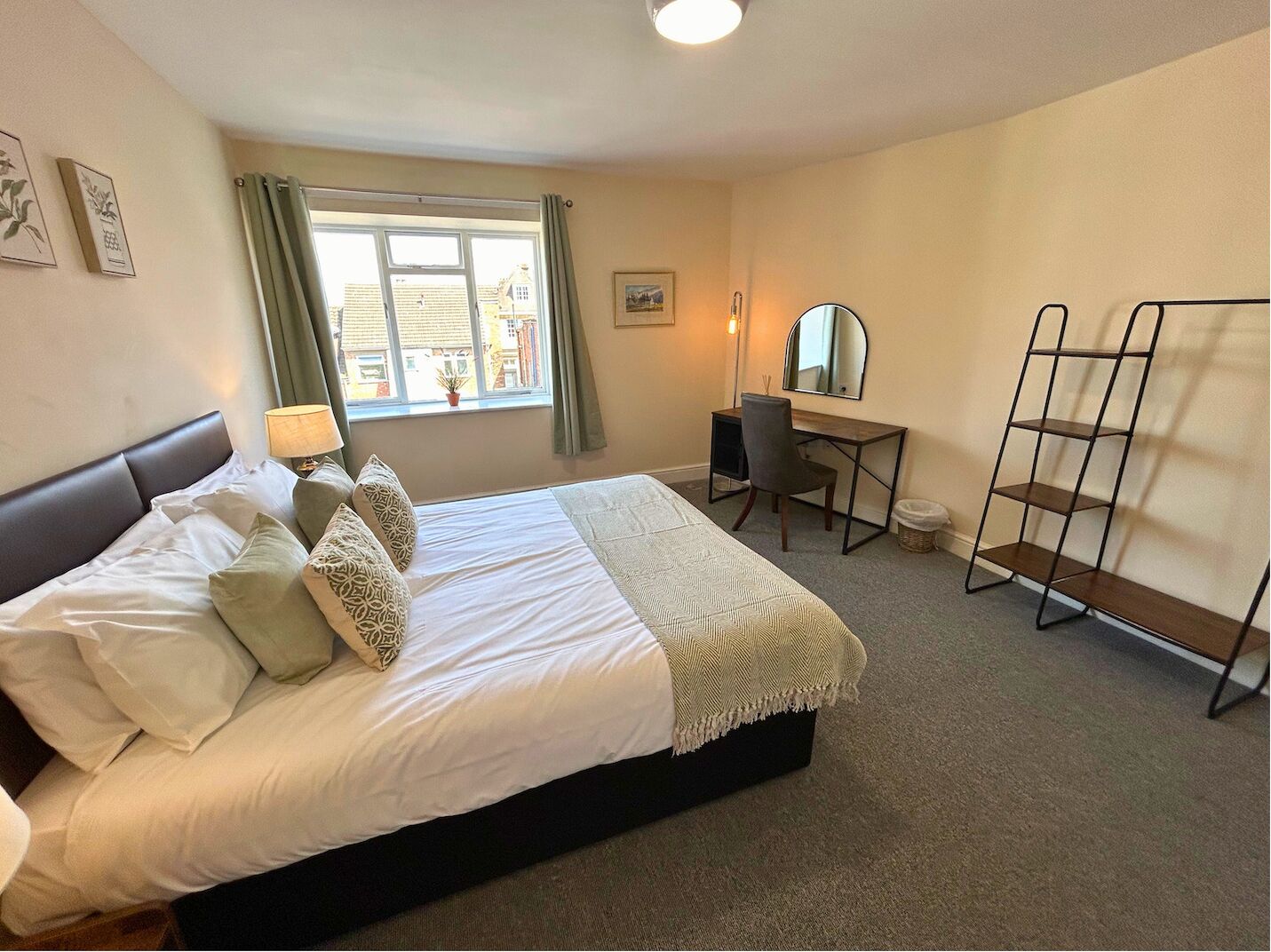 A bedroom with a bed, a desk, a chair, a mirror, and a shelf.